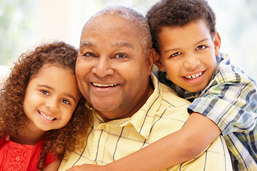 Smiling Grandfather in yellow shirt with grandson hugging his neck from behind and granddaughter in sitting in his lap