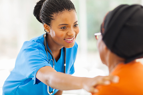 Nurse in blue scrubs smiling at patient with her hand on the patient's shoulder