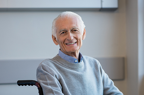 Elderly man in grey sweater sitting in wheelchair smiling